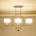 Modern brushed nickel island pendant light with three white fabric shades and crystal accents for dining room use