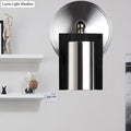 Modern brushed nickel wall sconce with metal shade and dark wood frame emitting warm white light for bedroom use