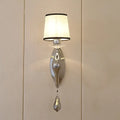 Elegant modern chrome wall lamp with cream fabric shade and dangling crystal pendant for living room use