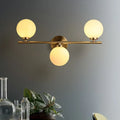 Brass-finished modern wall light with three white glass shades for bedroom featuring frosted glass globes