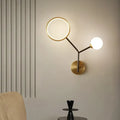 Modern gold and cream glass wall sconce lamp with circular ring light and spherical bulb on sleek brass base for bedroom lighting