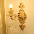 Modern gold wall mount light with ornate curved arm, crystal droplet pendants, and candle-style bulb for bedroom use
