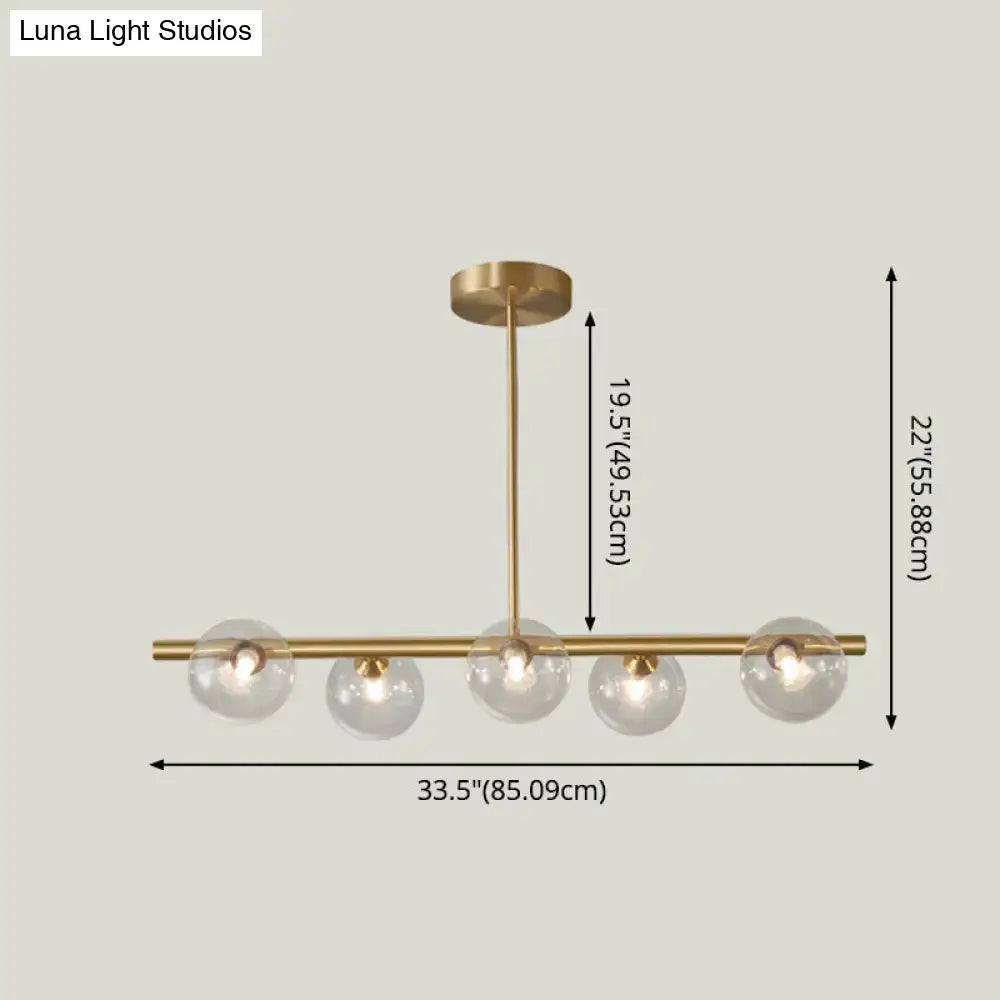 Modern gold island pendant lighting with brass finish and five clear glass globe shades for dining room island pendant lighting