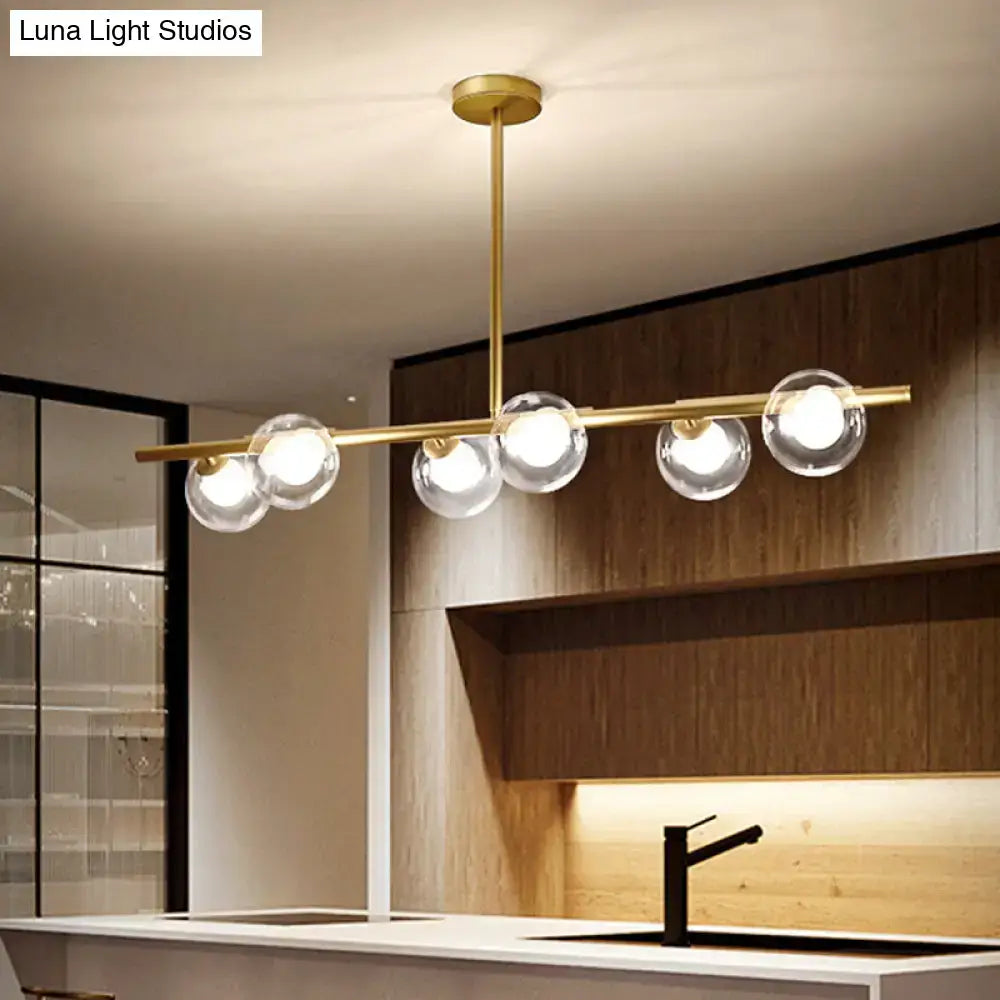 Modern gold linear island light fixture with five clear glass globe bulbs on a horizontal bar island light fixture