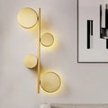 Modern gold vertical linear sconce light with four circular glowing fixtures in black gold finish for living room use