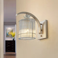 Modern gold wall mounted lamp with clear crystal shade and curved metallic arm for bedroom lighting