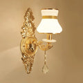 Modern ornate gold wall light with frosted glass shade and crystal teardrop designed as a bedroom sconce