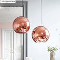 Two rose gold copper sphere pendant lights with polished surfaces hang from black cords for kitchen bar use