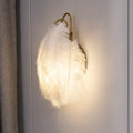 Modern white feather metal wall sconce with a luminous white feather and gold-toned metal frame for bedroom lighting