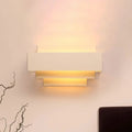 Modern white tiered rectangle wall lamp with layered stepped design emitting warm light for bedroom wall sconce use