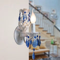 Modern white wall light with blue crystal draping featuring exposed bulb and dangling crystal droplets bedroom sconce