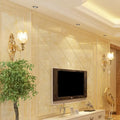 Modernist gold wall sconce with glass shade and direct wired electric next to a sleek black flat-screen tv on beige marble wall
