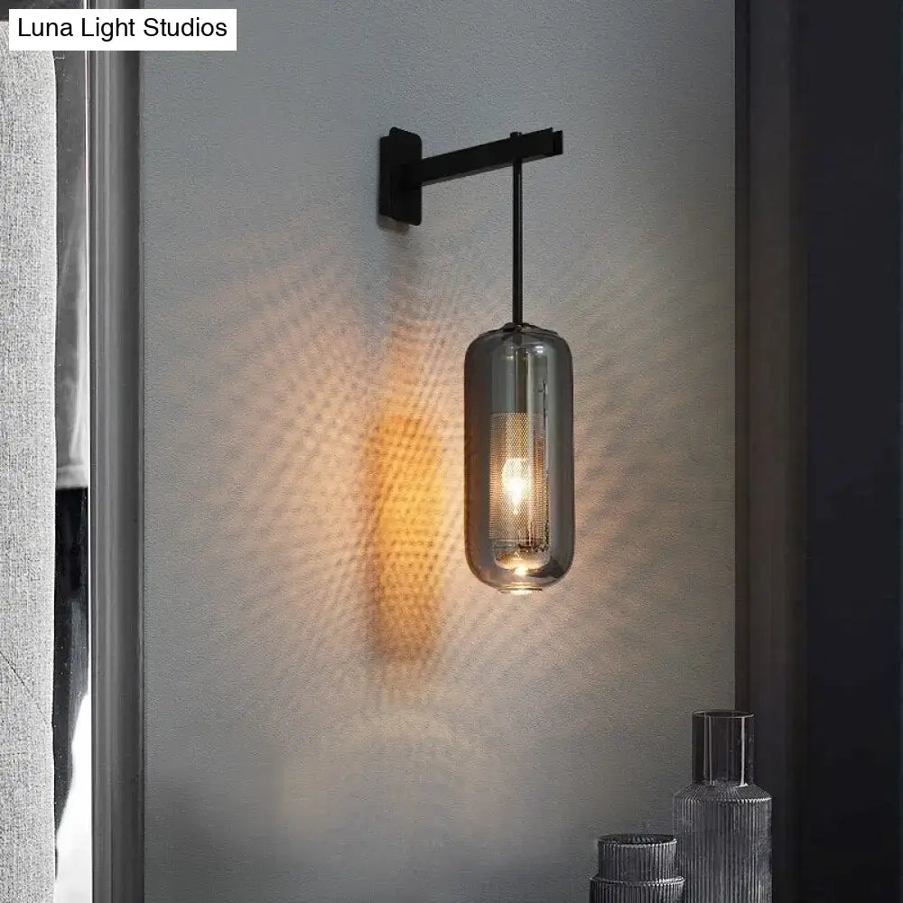 A sleek black metal nordic modern decor wall sconce with a cylindrical smoked glass lampshade and exposed filament bulb