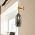 A post-modern wall-mounted brass sconce with smoke gray glass cylinder and internal spiral design for bedroom light