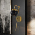 Postmodern black and gold swing arm wall sconce with clear spherical glass shade and adjustable arm for bedroom lighting