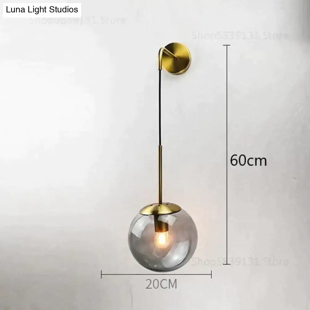 A brass-finished retro modern glass wall lamp with a smoked globe and curved arm for bedroom lighting