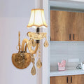 Traditional gold crystal wall sconce with fabric shade featuring warm illumination and dangling teardrop crystals